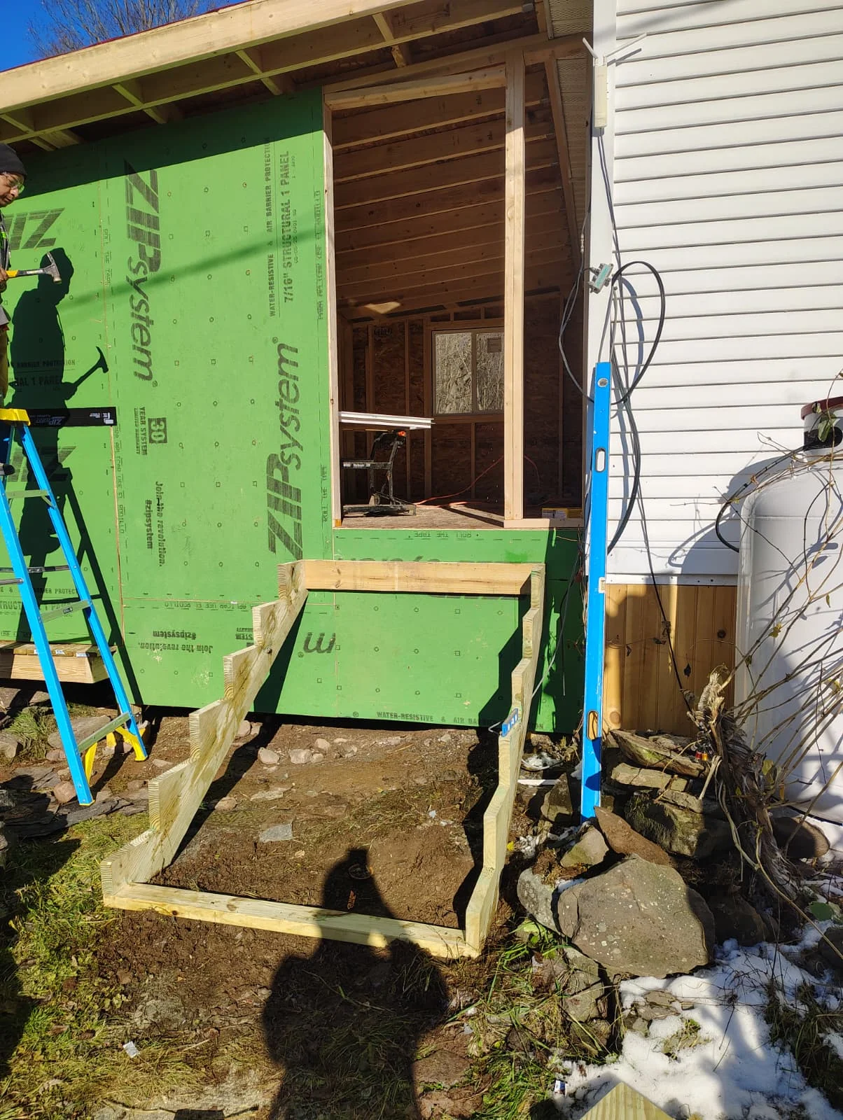 Wood-framed addition with green weather barrier, new window opening, and temporary bracing