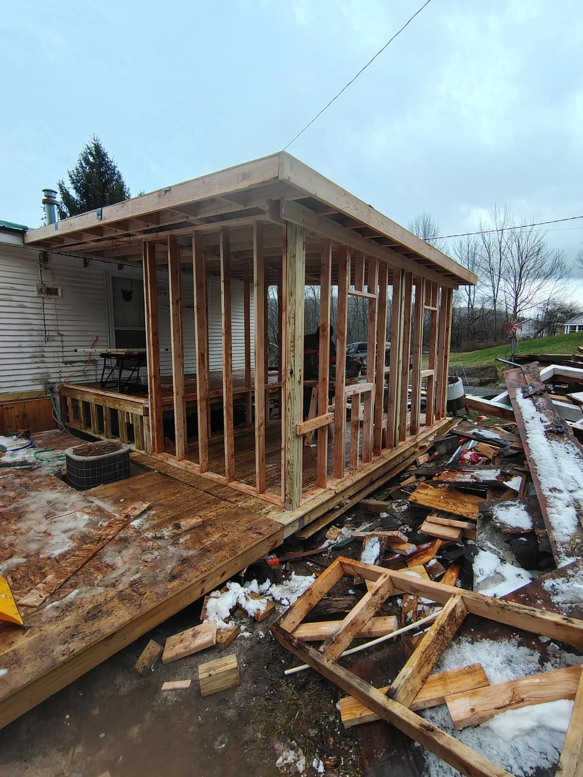 Wood-framed sunroom addition with casement windows and sloped roof under construction