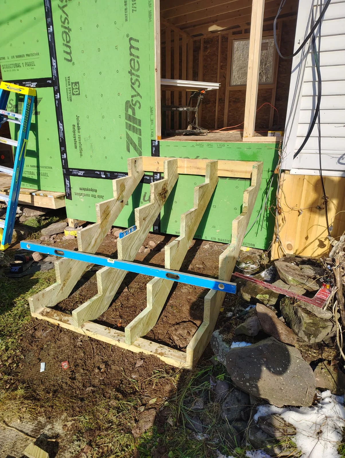 Pressure-treated wood foundation posts and beams with blue level on compacted soil base