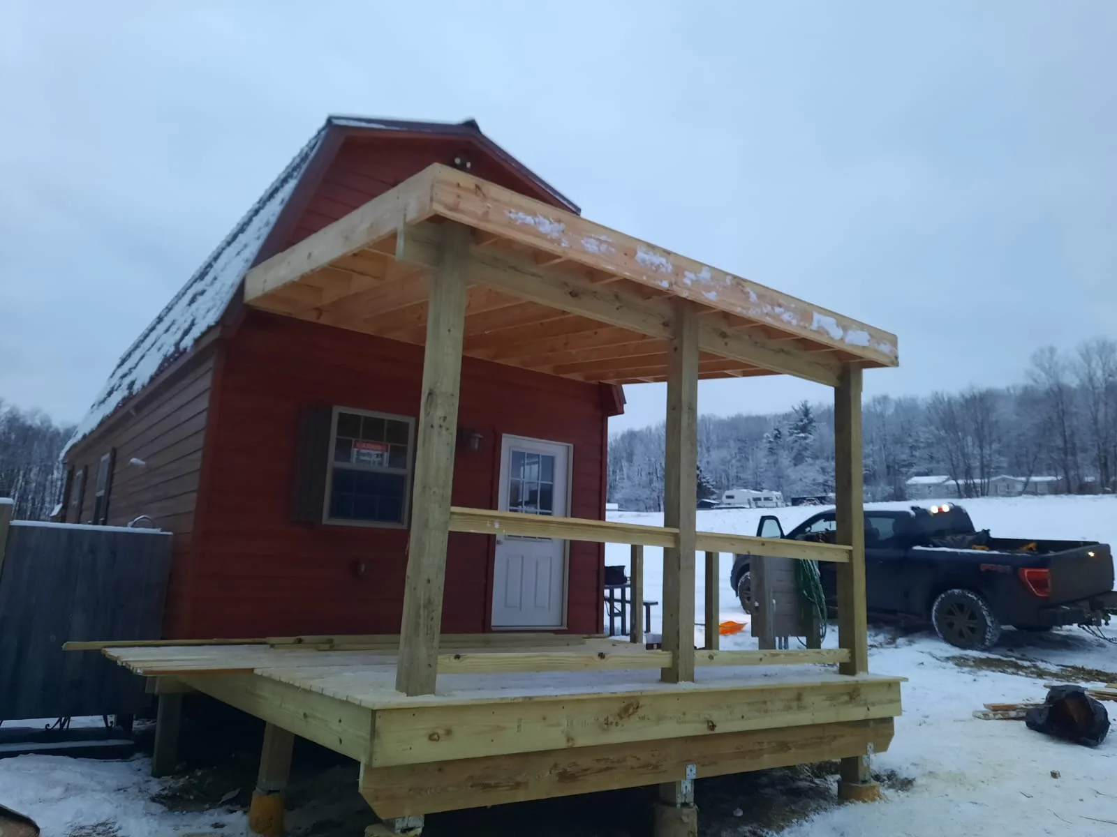 Pressure-treated wood porch with posts and decking attached to red cabin with gabled roof