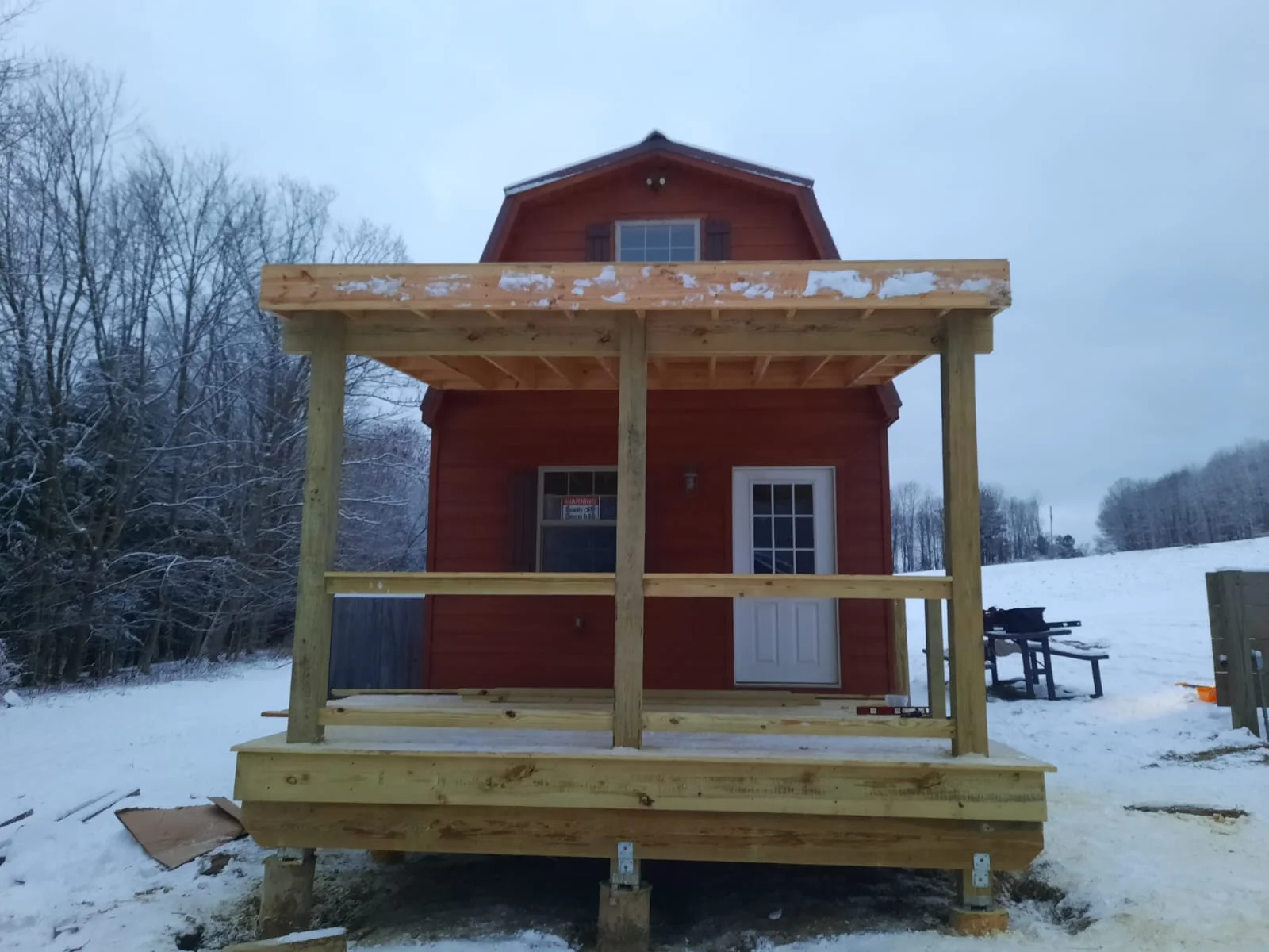Timber frame porch with pressure-treated posts, beams, and deck railing on red barn building