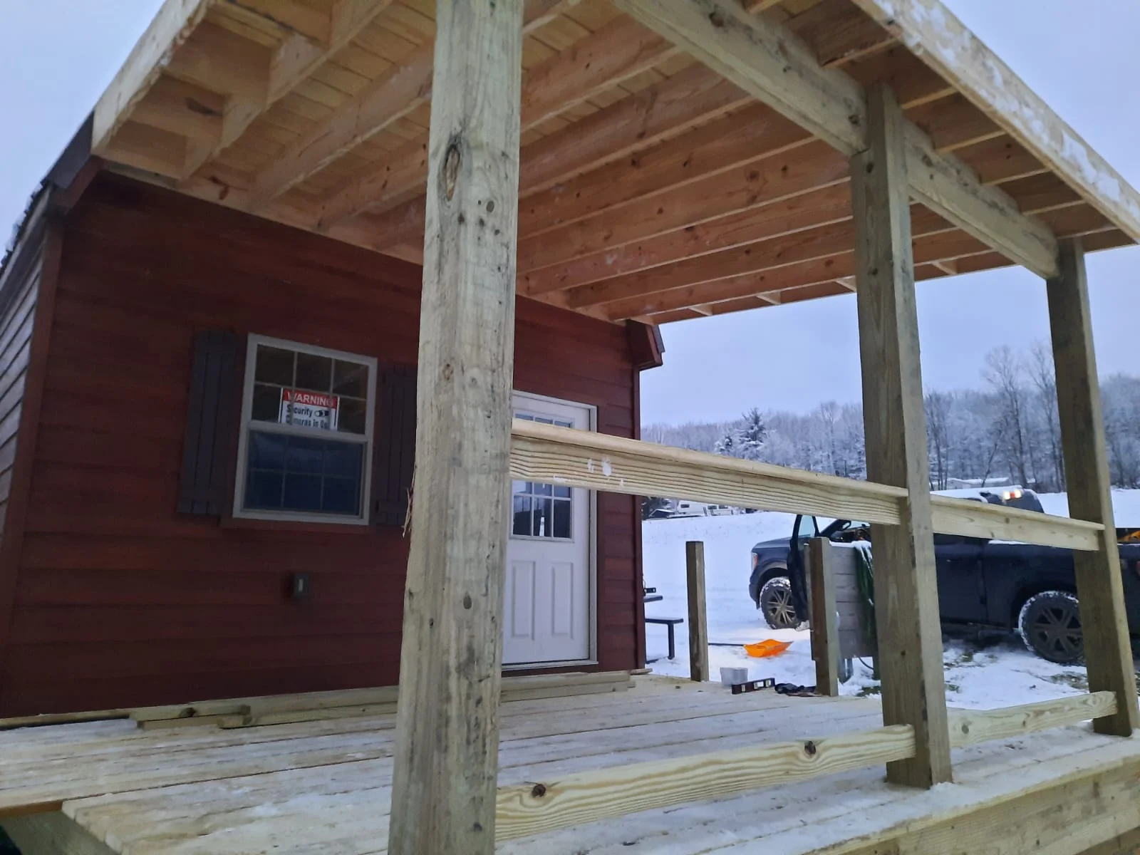 Post frame structure with timber posts, red wood siding, covered porch, and exposed beam ceiling