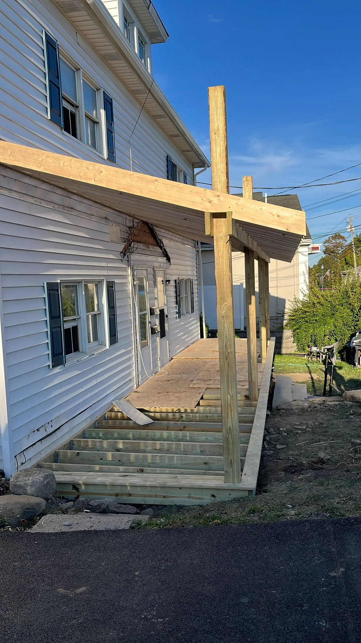 Newly constructed wood pergola and deck with vertical posts and horizontal beams attached to house