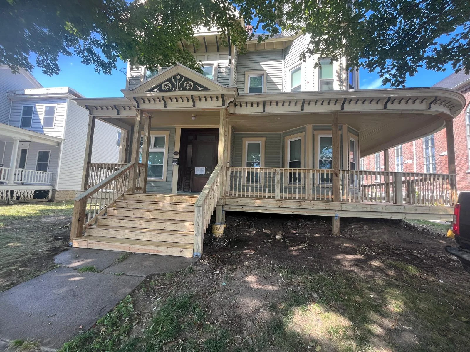 Restored Victorian porch with ornamental cornice, wood railings, and elevated deck on brick home
