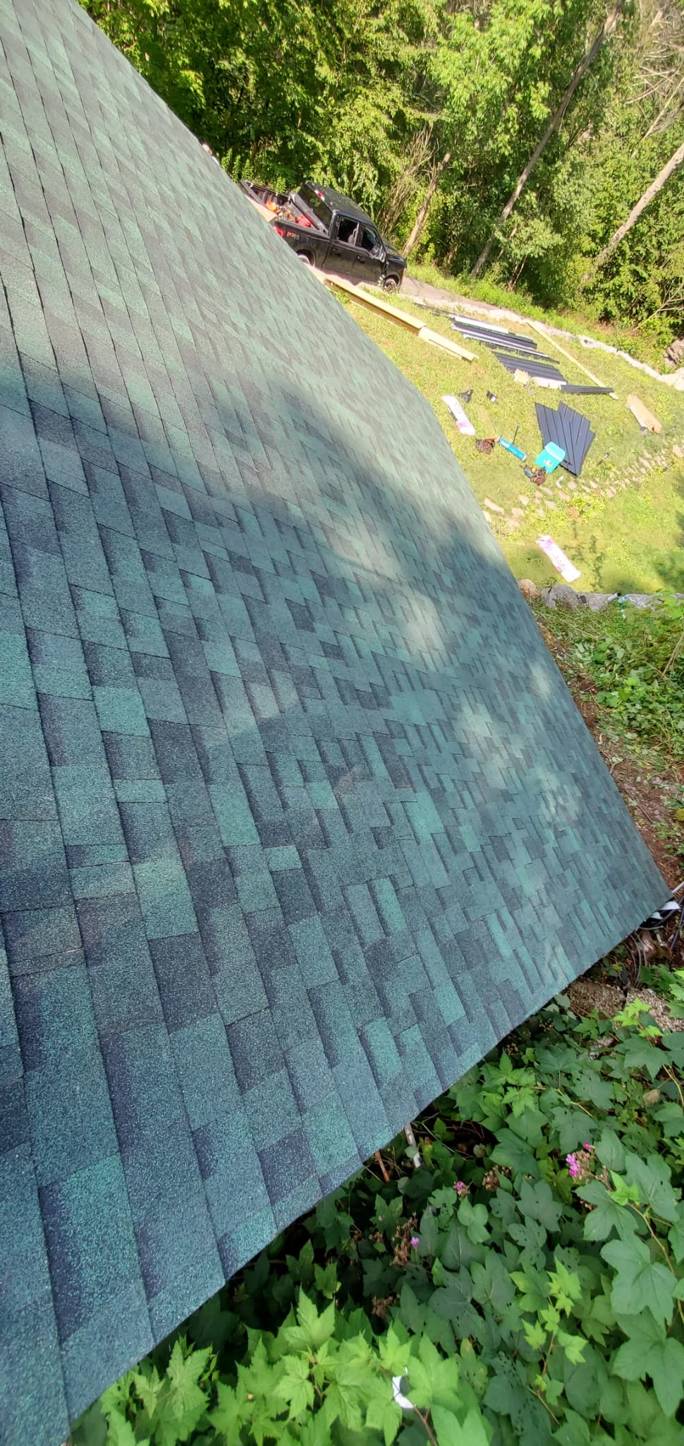 Steep-pitched roof with gray architectural shingles, installation in progress with materials staged below