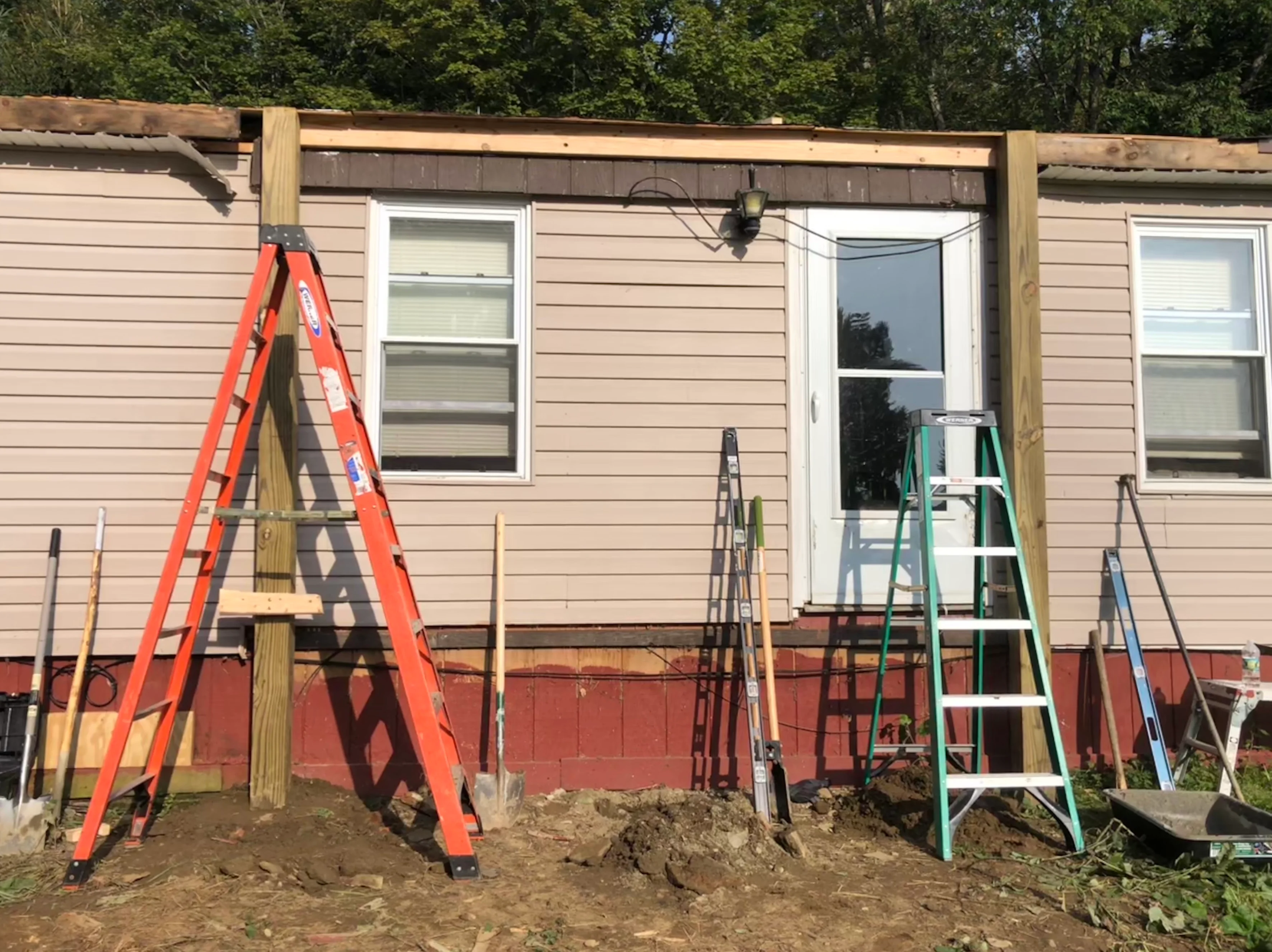 Mobile home siding replacement with tan horizontal lap siding, new white-framed windows, and red brick foundation